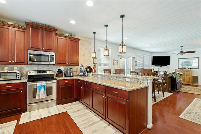 kitchen featuring open floor plan, stainless steel appliances, light wood-type flooring, and a peninsula