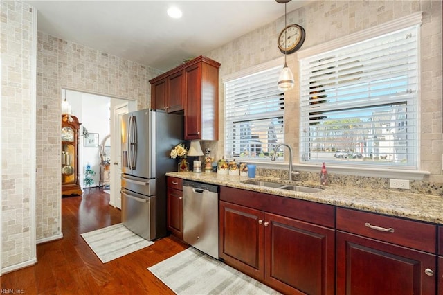 kitchen with appliances with stainless steel finishes, dark wood-type flooring, decorative light fixtures, light stone countertops, and a sink