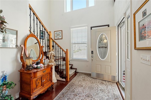 entrance foyer with dark wood finished floors, a towering ceiling, baseboards, and stairs