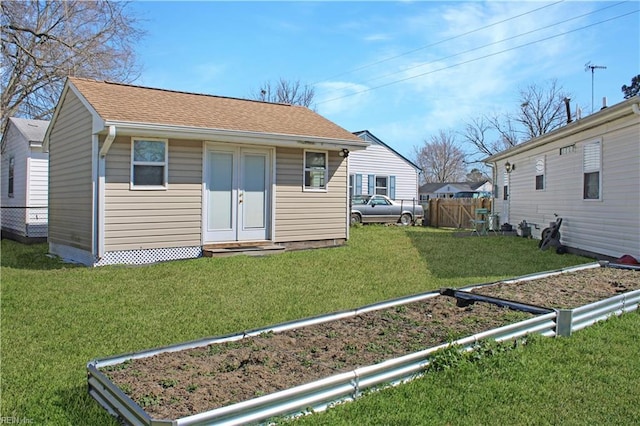 rear view of house with an outbuilding, roof with shingles, a yard, a vegetable garden, and fence