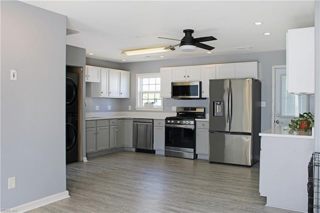 kitchen featuring stacked washer and dryer, light countertops, appliances with stainless steel finishes, light wood-style floors, and white cabinets