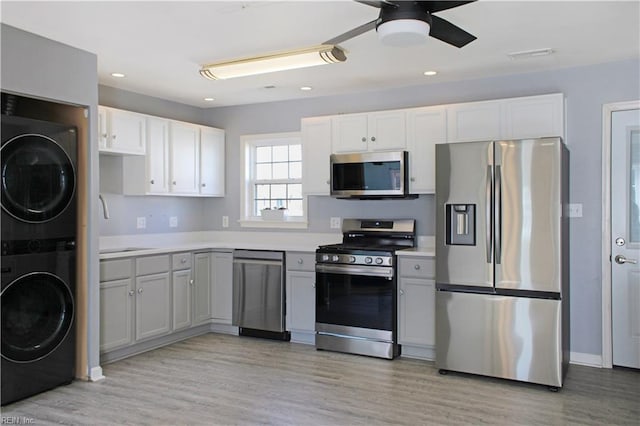 kitchen featuring light wood-style flooring, stainless steel appliances, a sink, light countertops, and stacked washer and clothes dryer