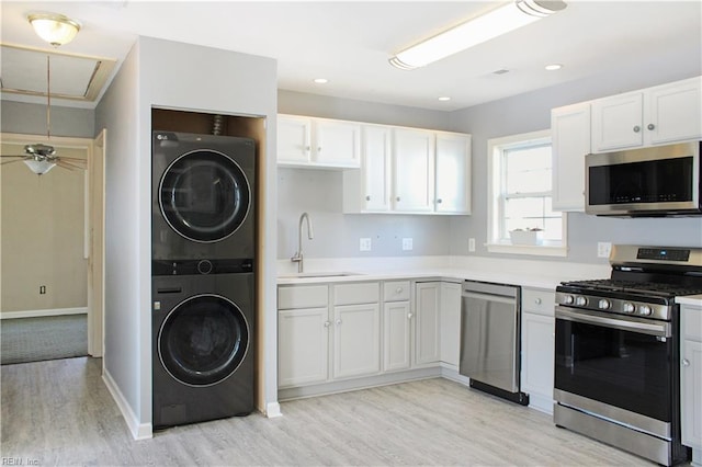 kitchen with appliances with stainless steel finishes, a sink, stacked washer and clothes dryer, and light wood-style floors