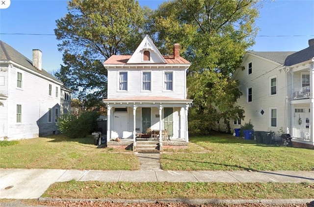 view of front facade featuring covered porch, a chimney, metal roof, and a front yard