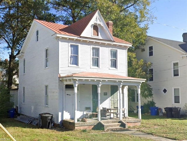 victorian home featuring a chimney, a porch, a standing seam roof, metal roof, and a front lawn