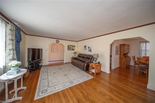 living area featuring baseboards, arched walkways, wood finished floors, and ornamental molding