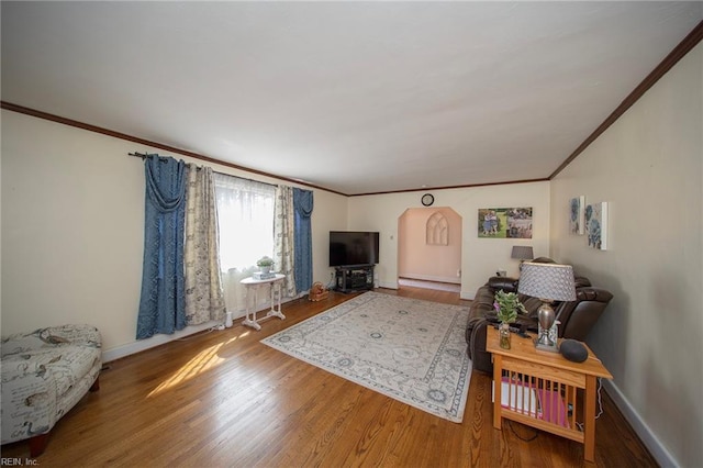 living area featuring arched walkways, a baseboard heating unit, wood finished floors, baseboards, and crown molding