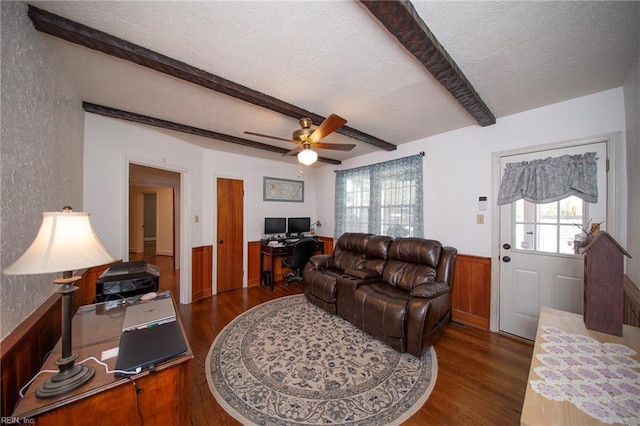 living room featuring dark wood-style flooring, a wainscoted wall, beamed ceiling, and a textured ceiling