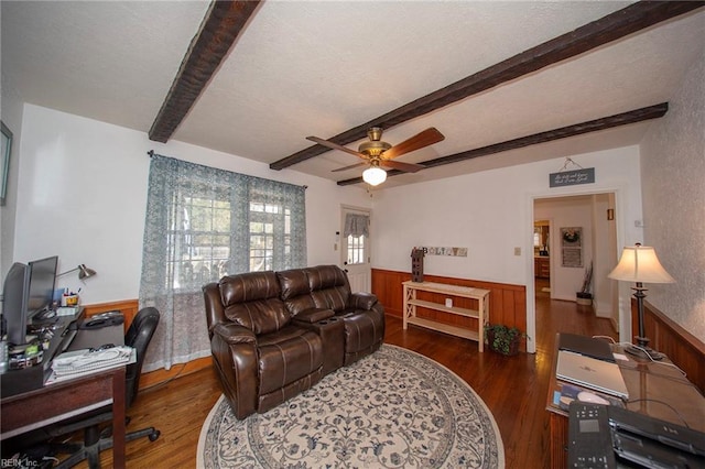 living area with ceiling fan, wood finished floors, beamed ceiling, and wainscoting