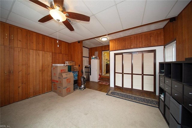 interior space with carpet flooring, ceiling fan, and wooden walls