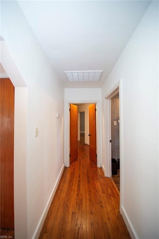 corridor with wood finished floors, visible vents, and baseboards