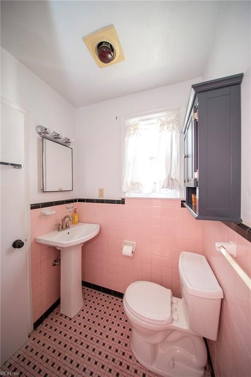 bathroom with wainscoting, a sink, toilet, and tile walls