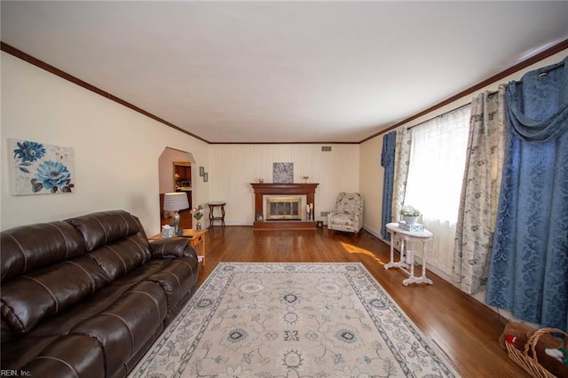 living room with arched walkways, ornamental molding, wood finished floors, and a glass covered fireplace