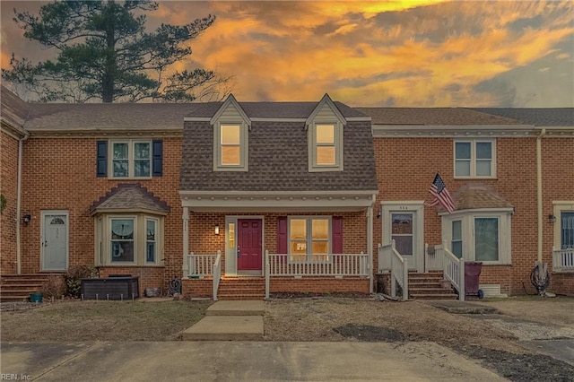 multi unit property featuring covered porch, a shingled roof, and brick siding