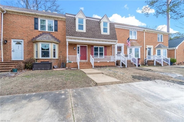 townhome / multi-family property with covered porch, brick siding, and a shingled roof