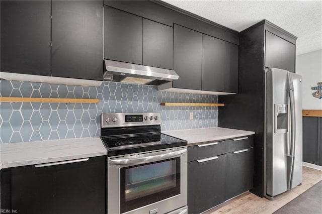 kitchen with stainless steel appliances, dark cabinets, backsplash, and under cabinet range hood