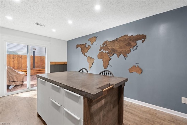 kitchen with baseboards, visible vents, dark countertops, a textured ceiling, and white cabinetry