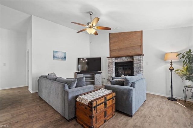 living area with light wood finished floors, a fireplace, a ceiling fan, and baseboards