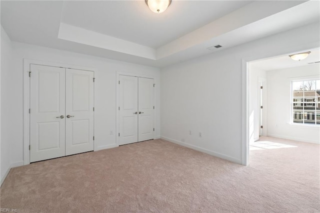 unfurnished bedroom featuring carpet floors, a raised ceiling, visible vents, and two closets