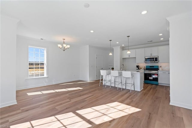 kitchen featuring appliances with stainless steel finishes, an island with sink, light wood-type flooring, and white cabinetry