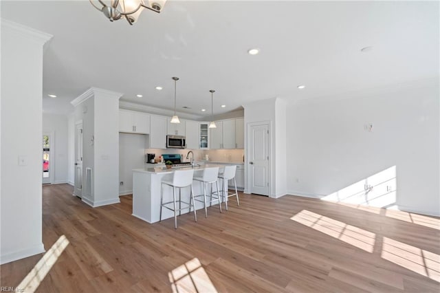 kitchen featuring a breakfast bar, light countertops, stainless steel microwave, ornamental molding, and an island with sink