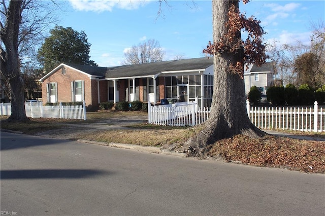 ranch-style home featuring a sunroom, a fenced front yard, and brick siding