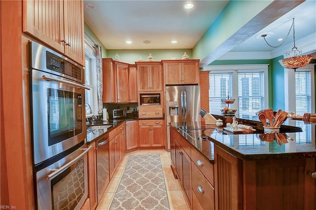 kitchen with light tile patterned floors, dark stone counters, a kitchen island, stainless steel appliances, and pendant lighting