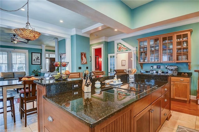 kitchen featuring open floor plan, ornamental molding, a center island, glass insert cabinets, and ornate columns