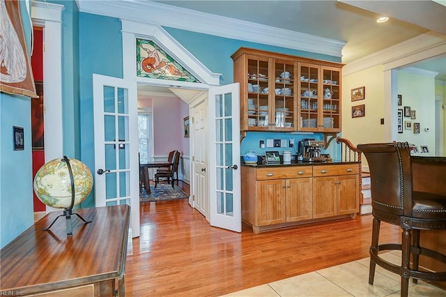 bar with light wood-type flooring, ornamental molding, and french doors