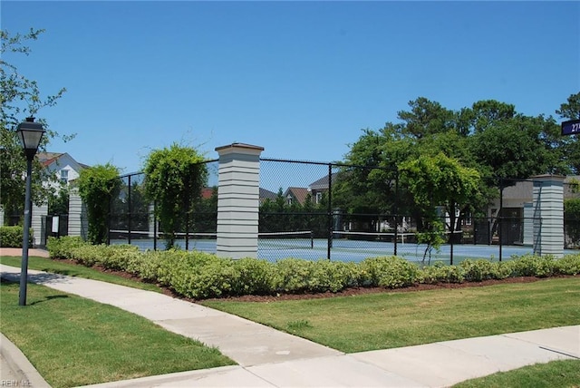 view of home's community featuring a tennis court, fence, and a lawn
