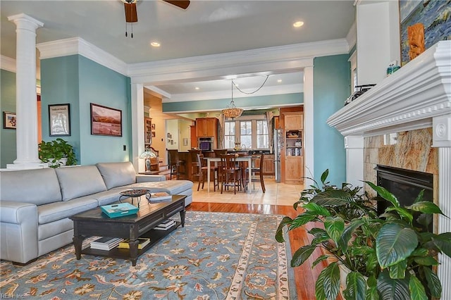 living area with a ceiling fan, a high end fireplace, ornamental molding, light wood finished floors, and ornate columns