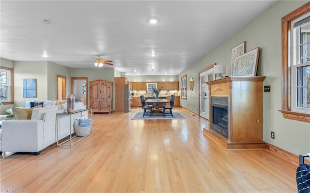 living room with light wood-type flooring, a fireplace, baseboards, and a ceiling fan