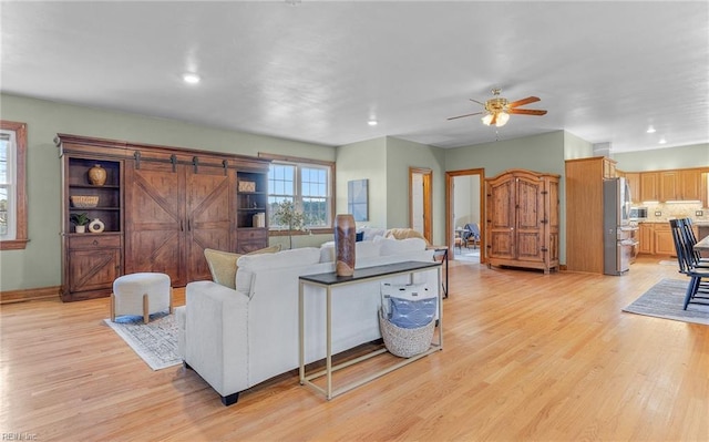 living room featuring a barn door, light wood-style flooring, a ceiling fan, and recessed lighting