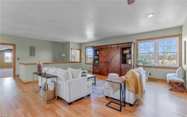 living room with a healthy amount of sunlight, a barn door, baseboards, and light wood-style flooring