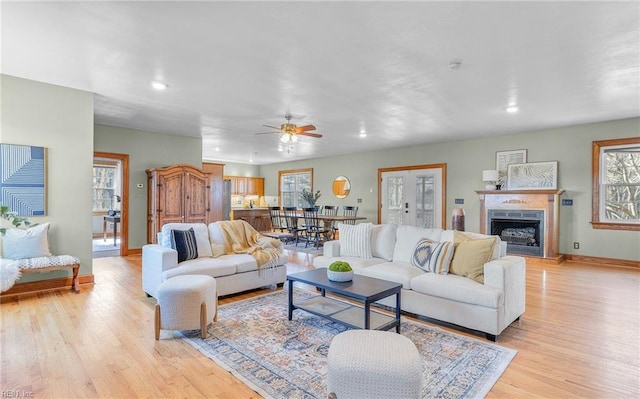 living room featuring recessed lighting, baseboards, a fireplace with raised hearth, and light wood finished floors