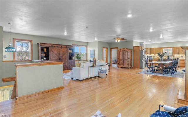 living room featuring light wood-style floors, a wealth of natural light, a ceiling fan, and a barn door