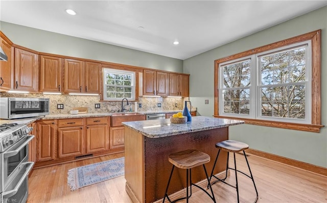 kitchen with a sink, appliances with stainless steel finishes, decorative backsplash, and light stone countertops