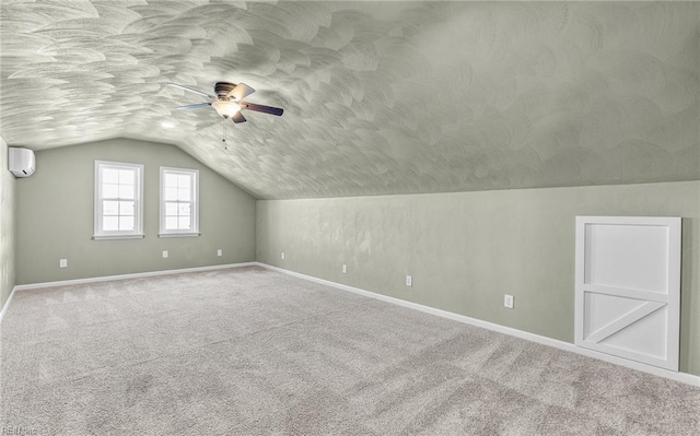 additional living space featuring a wall unit AC, carpet flooring, vaulted ceiling, a textured ceiling, and baseboards