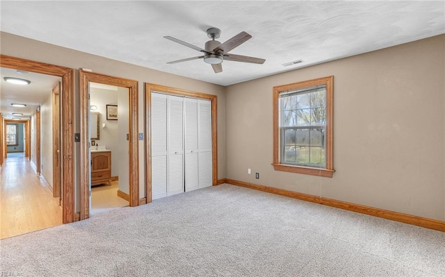 unfurnished bedroom featuring baseboards, visible vents, a ceiling fan, light colored carpet, and a closet