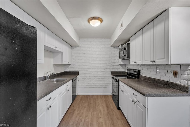 kitchen featuring dark countertops, light wood-style flooring, a sink, brick wall, and black appliances