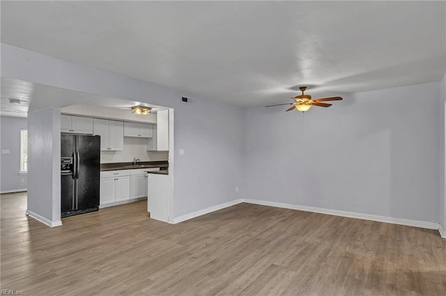 unfurnished living room with light wood-type flooring, a sink, a ceiling fan, and baseboards