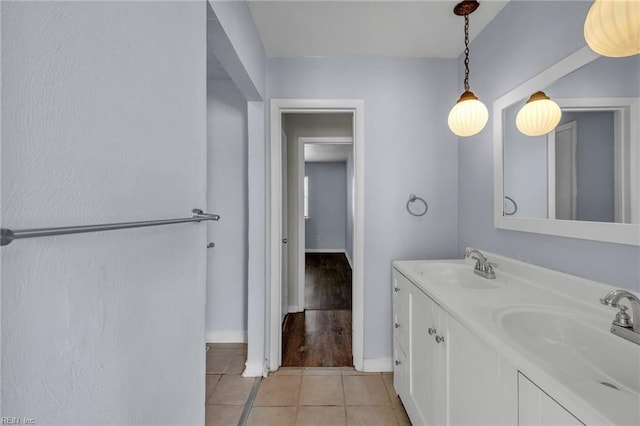 full bath with baseboards, double vanity, a sink, and tile patterned floors