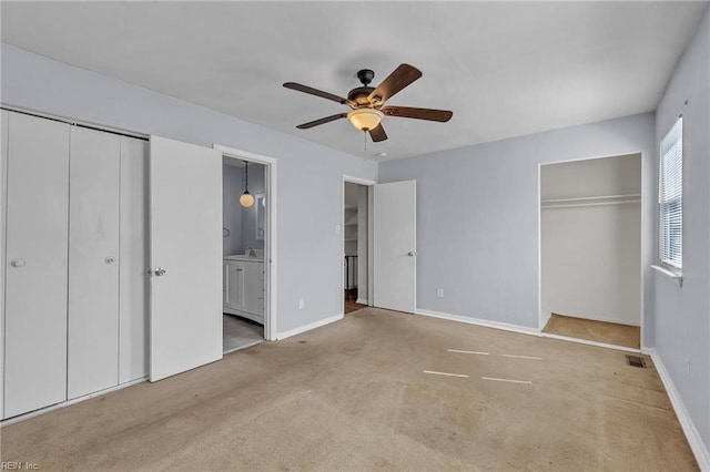 unfurnished bedroom featuring ensuite bathroom, carpet flooring, a ceiling fan, multiple closets, and baseboards