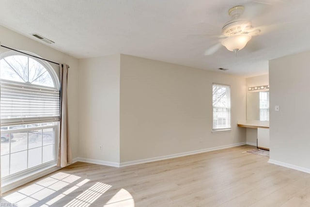 unfurnished room with a ceiling fan, light wood-type flooring, visible vents, and baseboards