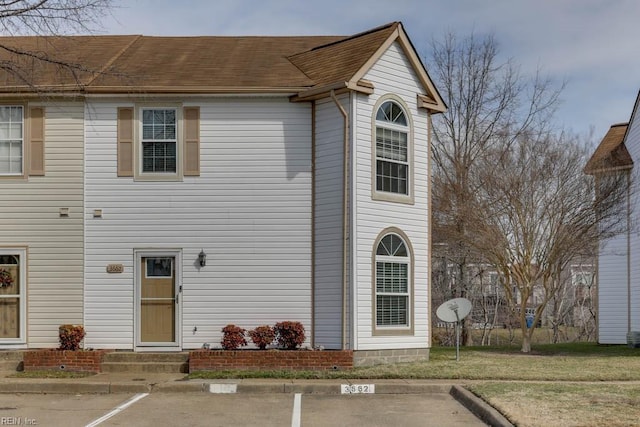 view of front of property with entry steps, uncovered parking, a shingled roof, and a front yard