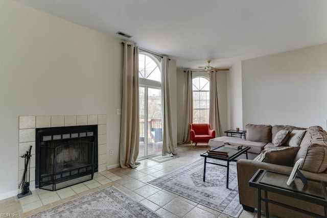 tiled living area with a ceiling fan, a tile fireplace, visible vents, and baseboards