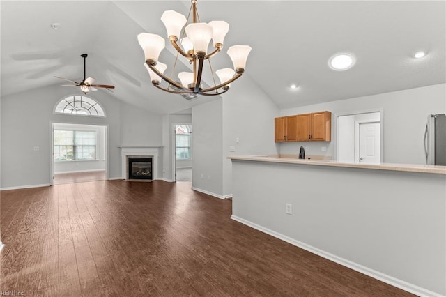 unfurnished living room with lofted ceiling, a fireplace with flush hearth, dark wood-style flooring, and ceiling fan with notable chandelier