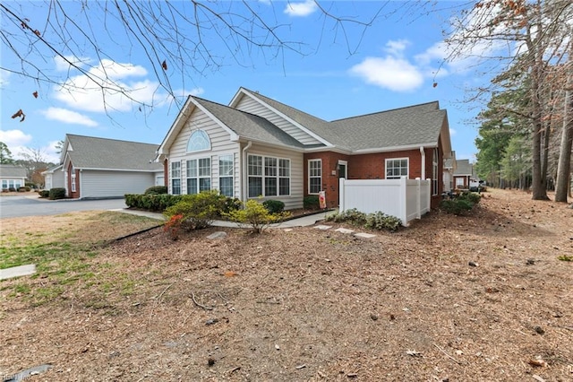 view of front of property featuring brick siding, fence, and roof with shingles