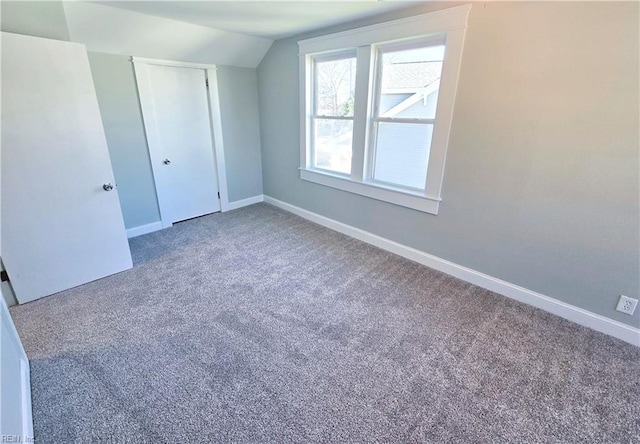 unfurnished bedroom featuring carpet, a closet, lofted ceiling, and baseboards