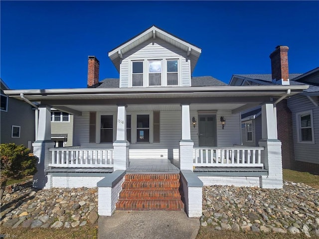 bungalow featuring covered porch, roof with shingles, and a chimney